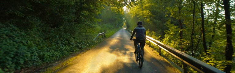 DRONE: Flying behind unrecognizable man riding his bicycle along empty road